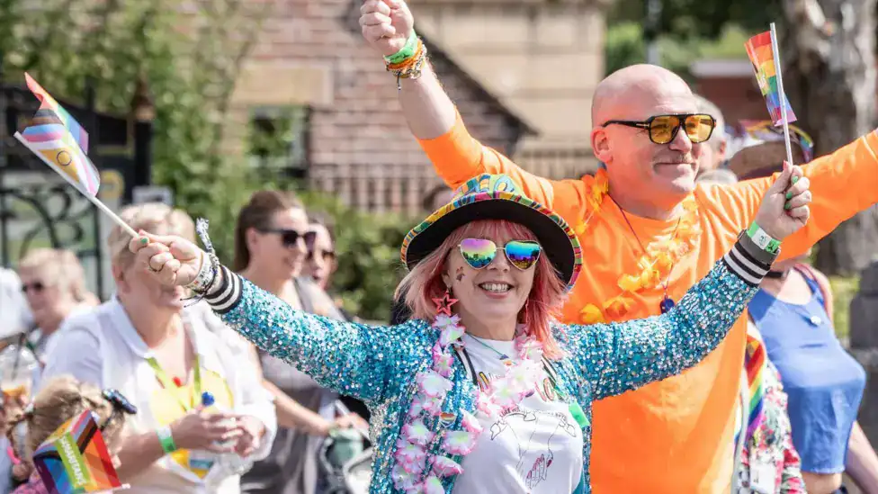 People celebrating Pride parade in Stafford with rainbow flags and colourful outfits.