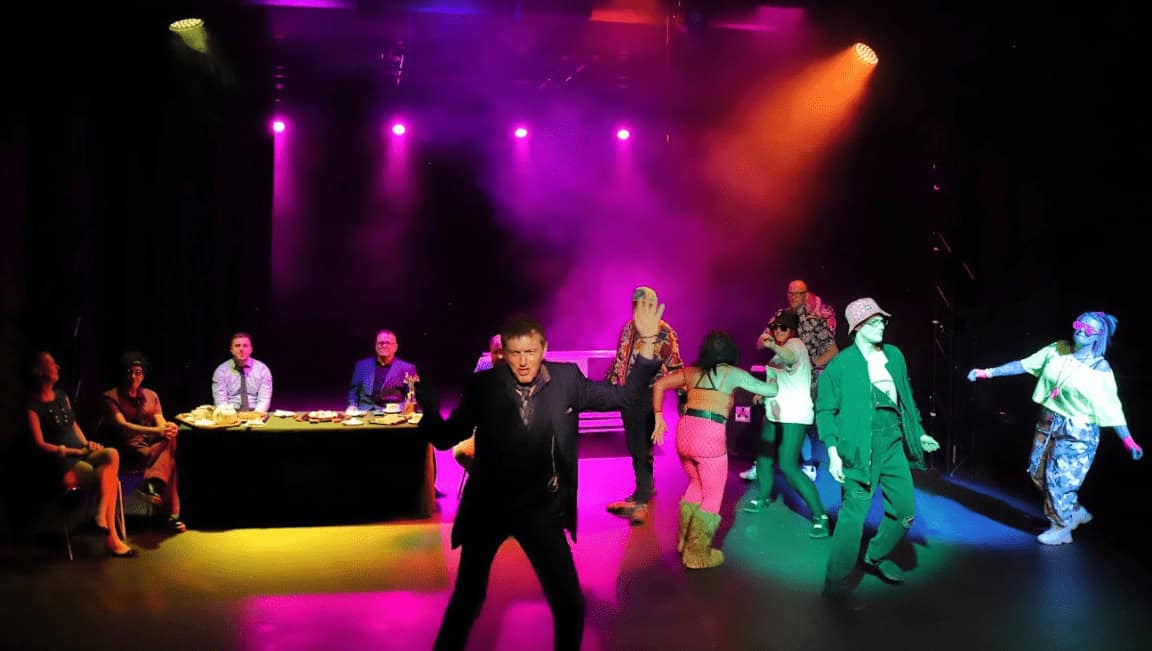 Group of performers dancing on stage with colourful lighting at Chase Recovery event.